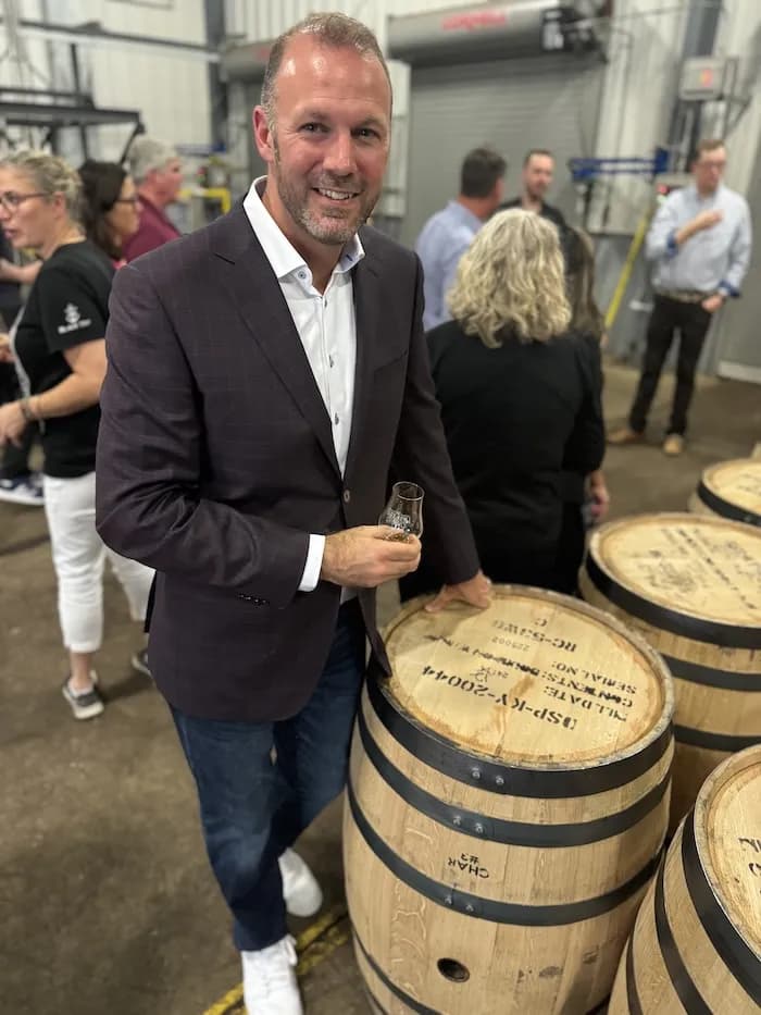 A man holding a tasting glass beside freshly filled barrels
